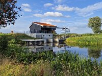 Pumping station to regulate water level of polder in Dutch province Friesland  Pumping station to regulate water level of polder in Dutch province Friesland : pumping station, pumping engine, regulate, regulating, water, water level, building, architecture, wooden, wood, canal, environment, environmental, rural landscape, rural, rural scene, non-urban landscape, non-urban scene, countryside, grass, green, tree, trees, sky, cloud, clouds, cloudy, blue, white, outside, outdoor, outdoors, no people, nobody, summer, summertime, day, daytime, de veenhoop, smallingerland, friesland, fryslan, netherlands, holland, dutch, europe, european